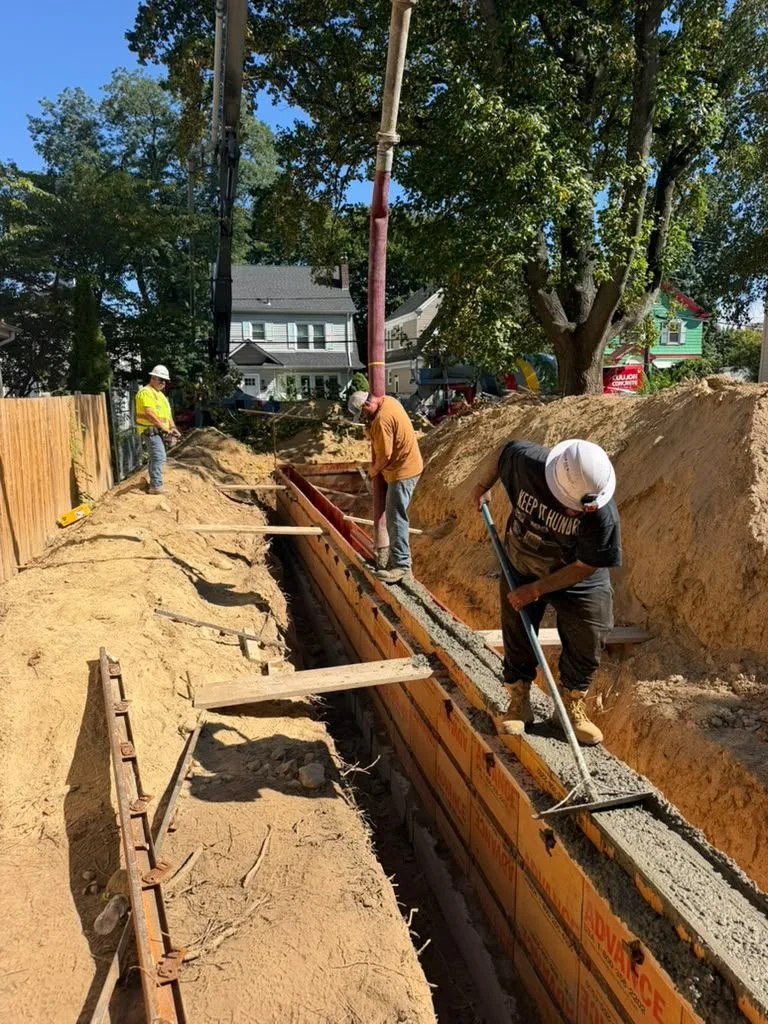 Crew guiding a pump hose into foundation forms during a pour