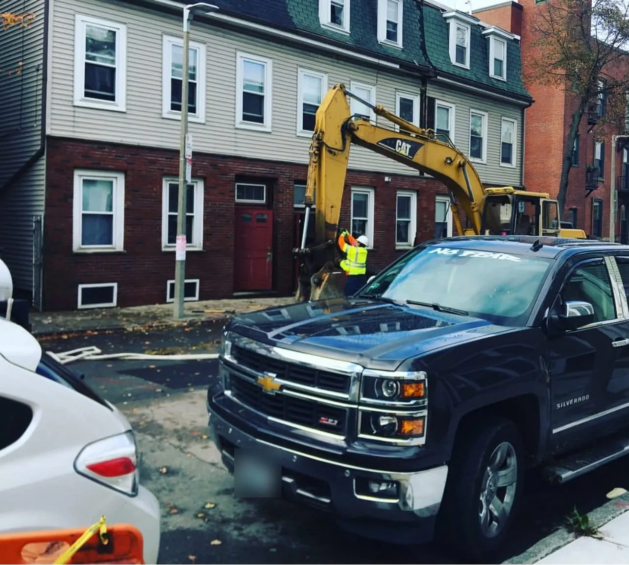 An excavator at work on a city street beside row houses