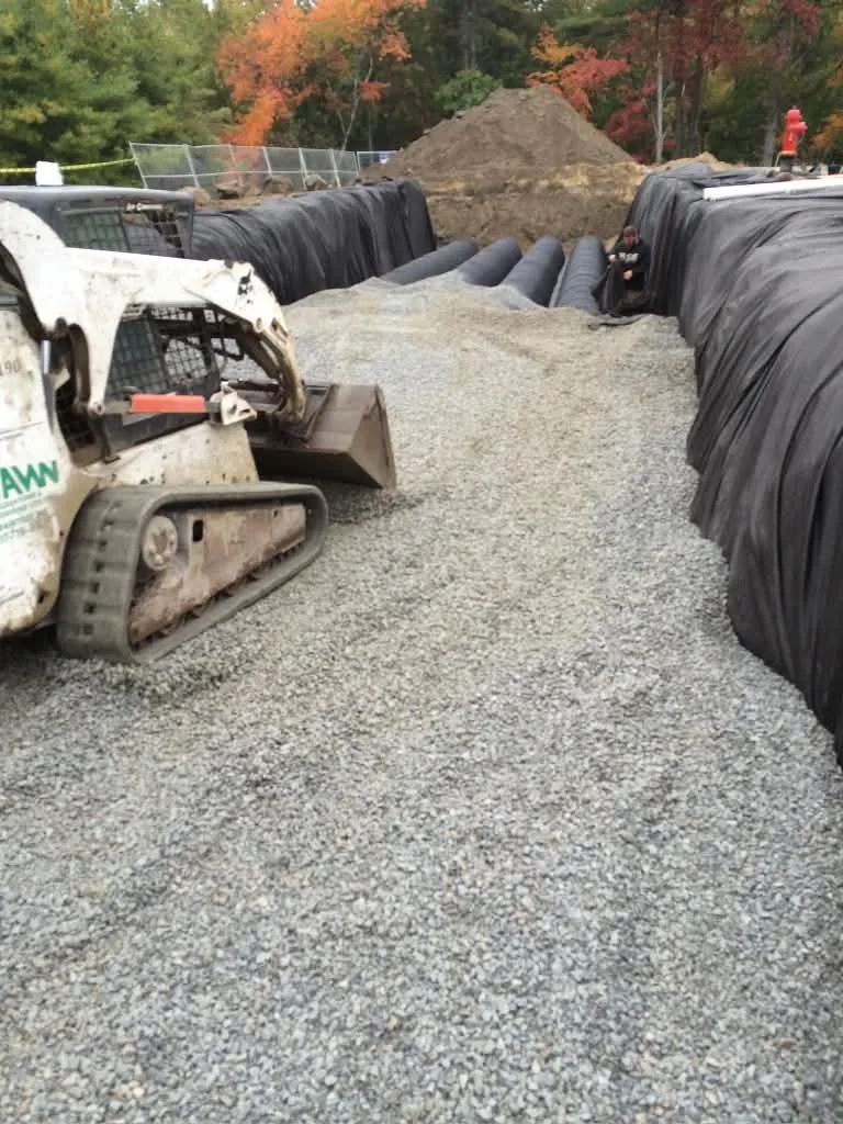 A skid steer spreading stone over drainage chambers
